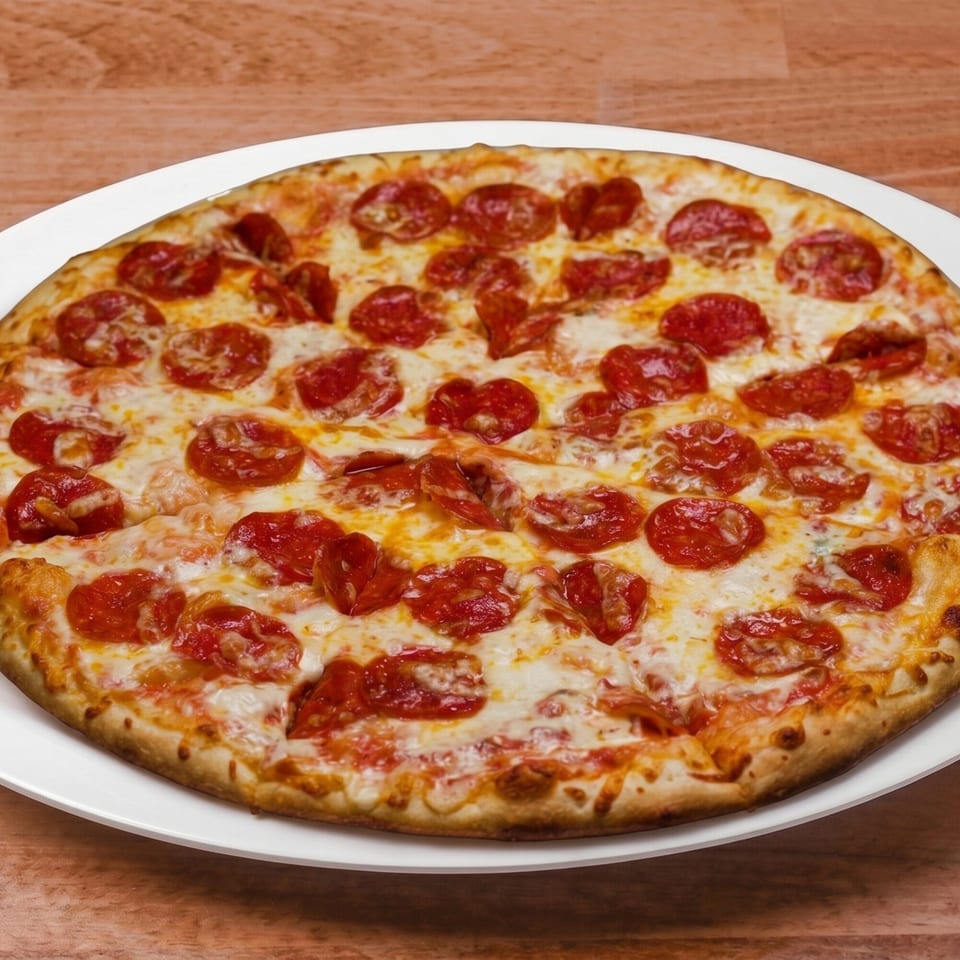 A whole pepperoni pizza with melted cheese on a white plate, on a wooden table.
