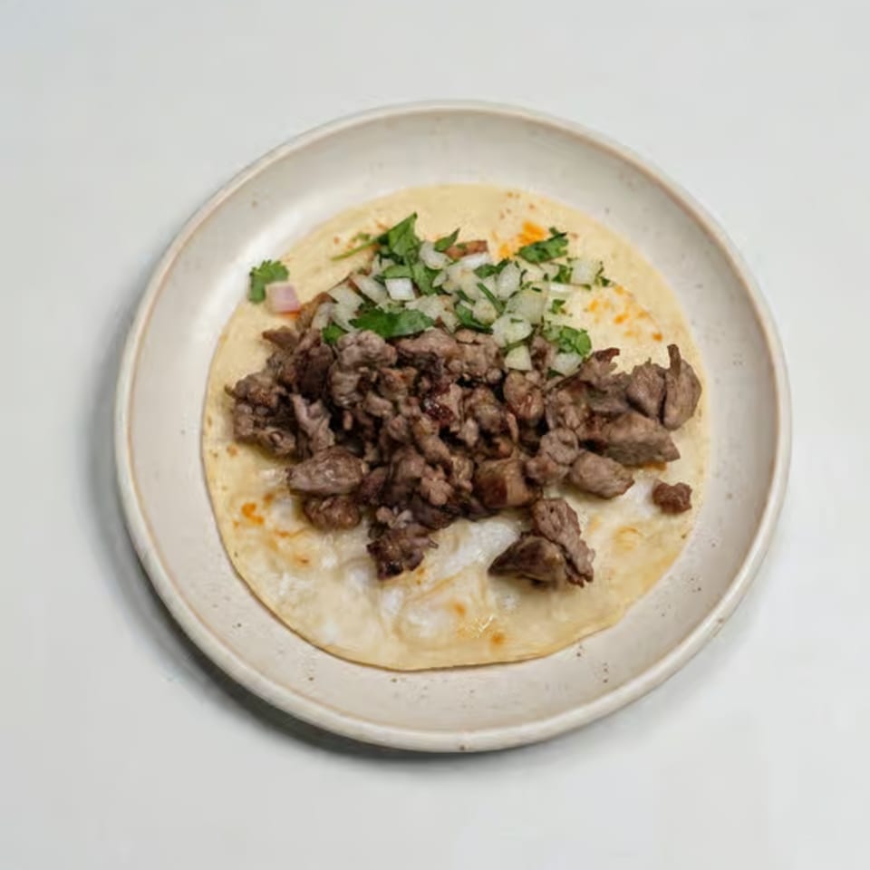 A single taco with chopped meat, diced onions, and cilantro on a white plate.