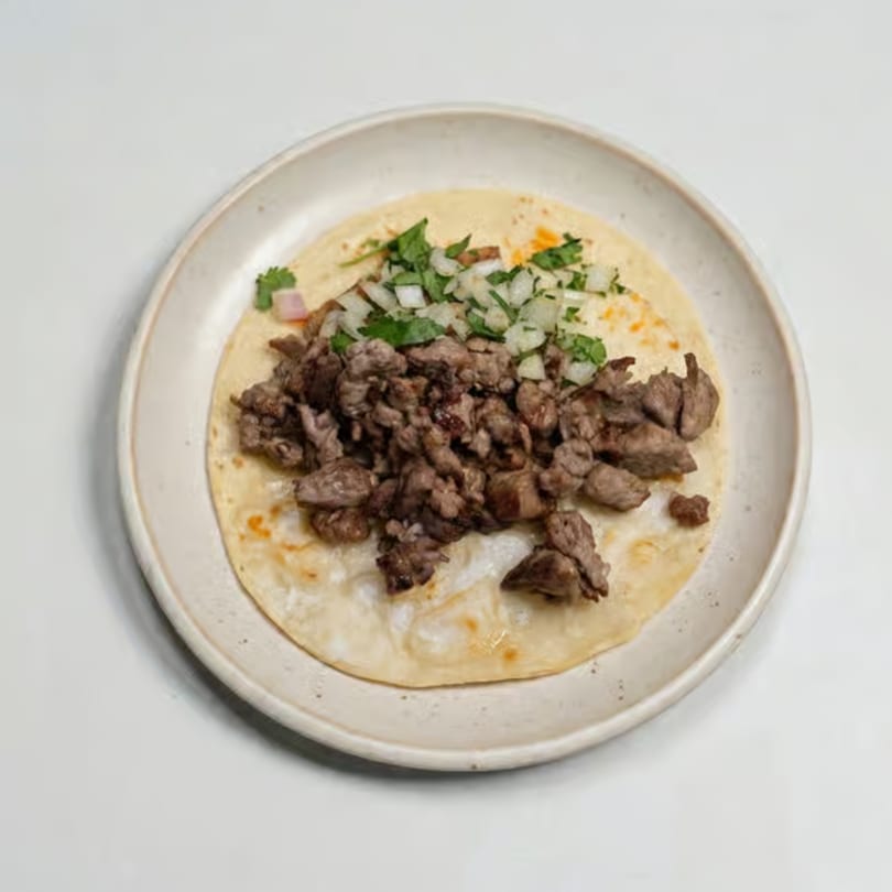 A single taco with chopped meat, diced onions, and cilantro on a white plate.